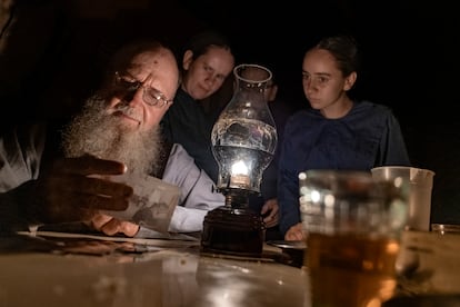 Henrique Loewen, with his daughters, looks at a photo of his old friend, Isaac Peter, by candlelight; Peter has a fatal melanoma. 