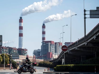 Un motociclista pasa frente a las chimeneas humeantes de una central de generación eléctrica en Shaghái (China).
