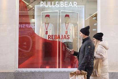 Dos personas caminan delante de un escaparate anunciando las rebajas, este domingo en Madrid.