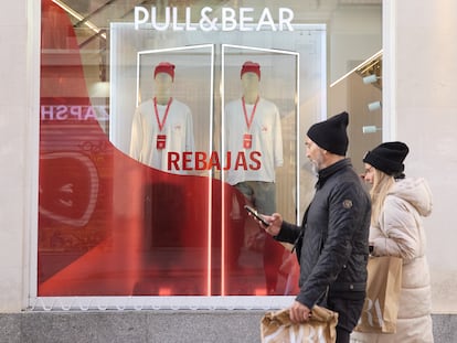 Dos personas caminan delante de un escaparate anunciando las rebajas, este domingo en Madrid.