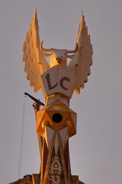 La figura alada del evangelista Lucas, representada por buey, en lo alto de su torre, en una imagen tomada al amanecer, justo en el intervalo de tiempo en el que el mármol blanco toma un tono anaranjado. En la imagen se aprecian también las iniciales, realizadas con 'trencadís'.