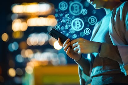 Mid-section of young Asian woman using smartphone in city at night, against illuminated street lights bokeh, working with Bitcoin technologies, investing or trading Bitcoin on cryptocurrency. Business on the go