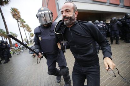 Um agente policial leva um cidadão para fora do perímetro de segurança formado ao redor das escolas.