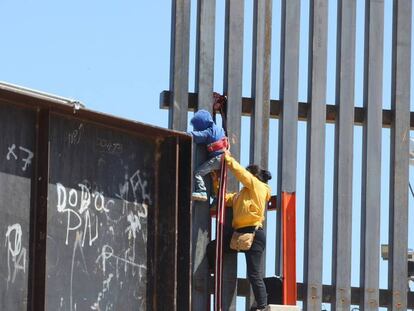 Una mujer ayuda a su hijo a trepar la valla fronteriza que divide a México y Estados Unidos.