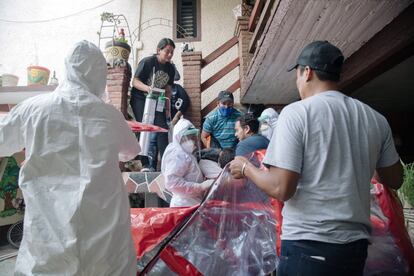 Los Sánchez Luna, junto a los hijos del enfermo, preparan al hombre para ingresarlo en una de las ocho cápsulas para los pacientes de coronavirus facilitadas por la Administración del Valle de Chalco a la estación de bomberos. El paciente, al que bajaban por las escaleras del domicilio con mucha dificultad, había perdido el conocimiento.