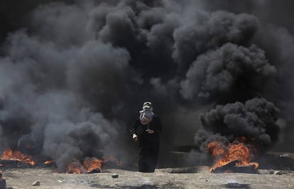 Uma mulher caminha pela fumaça gerada pela queima de pneus durante o protesto na fronteira entre Gaza e Israel.