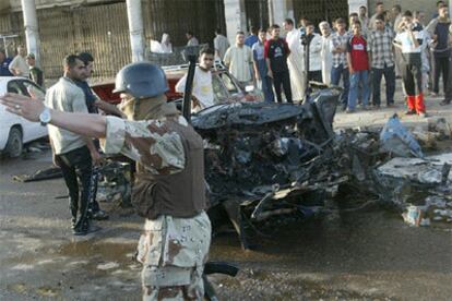 Un policía vigila la zona donde ha explotado un coche bomba, ante la mirada de un grupo de ciudadanos, en un bariro de Bagdad.