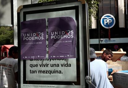 Unos obreros curran detras de un cartel de la coalición Unidos Podemos cerca de la sede del Partido Popular en Madrid.