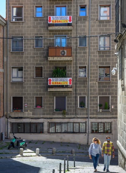 Una pareja pasea por una calle cercana a la Plaza Mayor donde se puede leer un cartel que denuncia un piso turístico ilegal en 2019.