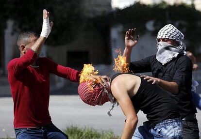 Dos jóvenes intentan apagar las llamas de la cabeza de un manifestante en Hebrón.