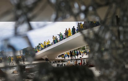 Supporters of Brazil's former President Jair Bolsonaro are pictured through broken glass as they hold a demonstration against President Luiz Inacio Lula da Silva, in Brasilia on January 8, 2023. 