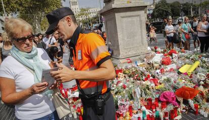 Un agente c&iacute;vico atiende a una mujer frente al altar improvisado en La Rambla en homenaje a las v&iacute;ctimas.