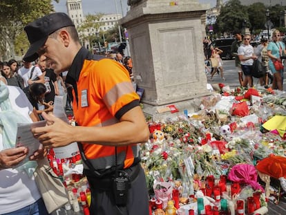 Un agente c&iacute;vico atiende a una mujer frente al altar improvisado en La Rambla en homenaje a las v&iacute;ctimas.