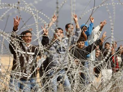 Un grupo de palestinos hacen gestos de victoria junto a una alambrada de la frontera entre el sur de Gaza e Israel.