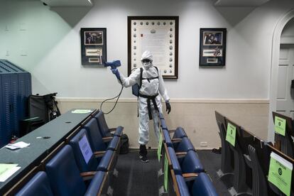 Un miembro del personal de limpieza, vestido con un traje protector, rocía con desinfectante la sala de prensa de la Casa Blanca.