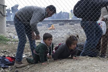 Un padre ayuda a sus hijos a escapar de la policía en Macedonia rompiendo la red metálica de la frontera cerca de la localidad griega de Idomeni.