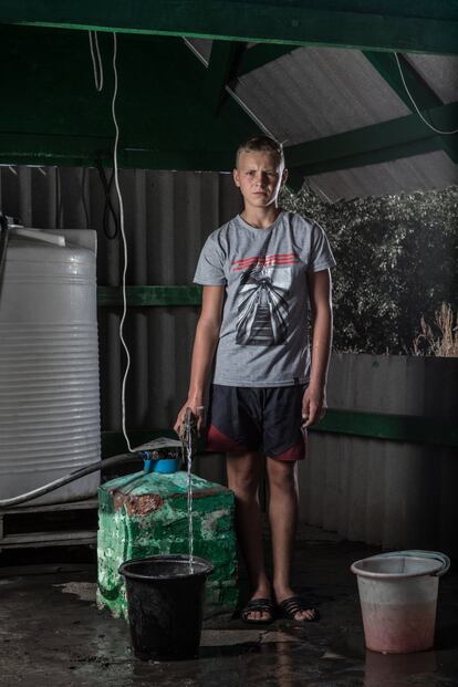 Edik Gorbulin, de 13 años, llena un cubo con agua en Bakhmutka, en la región de Donetsk (Ucrania). Edik vive con sus padres y su hermana Elizaveta. La escuela en la que estudiaba fue destrozada por un bombardeo. “No hay otros chicos con quien jugar”, dice. “Ya no es lo mismo. Antes había otros seis chavales que vivían en mi bloque, pero se fueron todos en 2014”. Ahora ocupa parte de su tiempo ayudando a su madre y su hermana con la colección de agua. “Me siento cansado, pero tengo que ir al pozo a por el agua. Es un trabajo duro para mi madre”, dice.