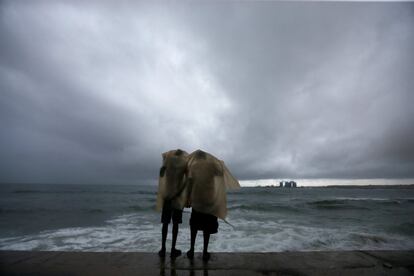 Dos hombres usan un plástico para protegerse de la fuerte lluvia de los monzones mientras permanecen junto al mar en Colombo (Sri Lanka).