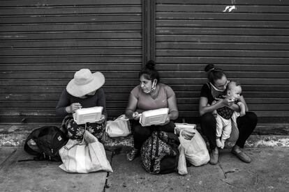 Las peruanas Olga Condori (29 años) y Alicia Trujillo (33 años), junto a la venezolana Mariela del Valle (23 años), que da de comer a su bebé de cinco meses, conversan sentadas mientras almuerzan la comida que les dio la Municipalidad de Lima. Ninguna de las tres tiene dinero para pagar el alquiler del espacio en el que viven o para comprar comida, y esperan que termine pronto el confinamiento para poder salir a trabajar y generar ingresos.