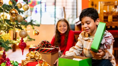 Unos niños abriendo regalos junto al árbol de navidad.