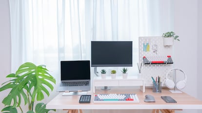 Una escritorio en una habitación con una planta a su lado y una ventana detrás.