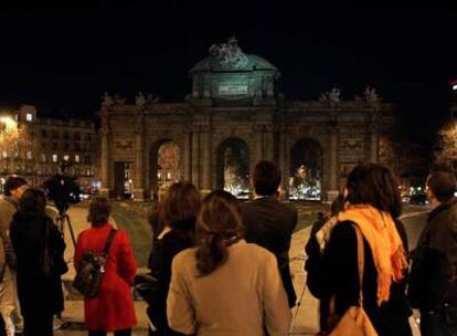 Un grupo de personas observa la Puerta de Alcalá de Madrid a oscuras durante el apagón.