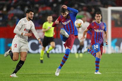 Piqué despeja el balón ante la presión de Rafa Mir durante el partido en el Pizjuán