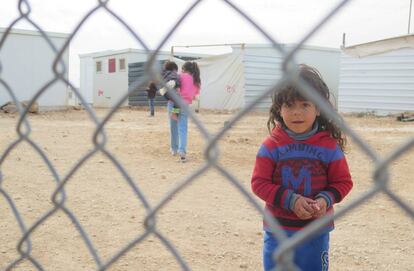 Una niña mira a cámara al otro lado de la verja del campo de refugiados de Zaatari, en Jordania.