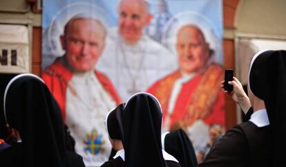 Varias monjas observan y fotografían un panel con la imagen de varios pontífices.