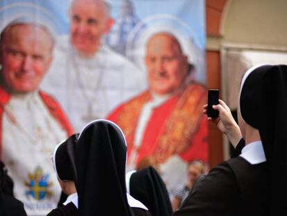 Varias monjas observan y fotografían un panel con la imagen de varios pontífices.