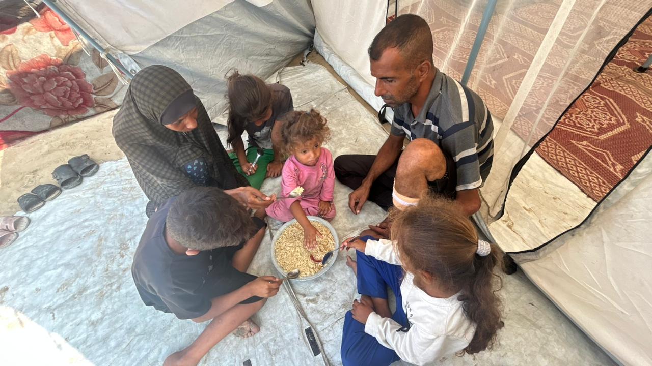 La familia Siyam comparte un plato de comida en su precaria tienda de campaña en el campo de refugiados de Nuseirat, en el centro de Gaza, a principios de noviembre de 2025.