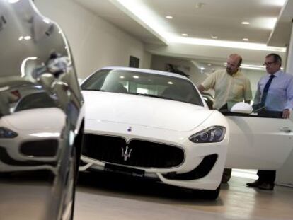 Un vendedor (izquierda) muestra un Maserati a un posible comprador en un concesionario.