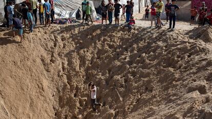 Civiles palestinos contemplan el boquete causado por una bomba en el campo de refugiados de Jan Yunís, en Gaza.