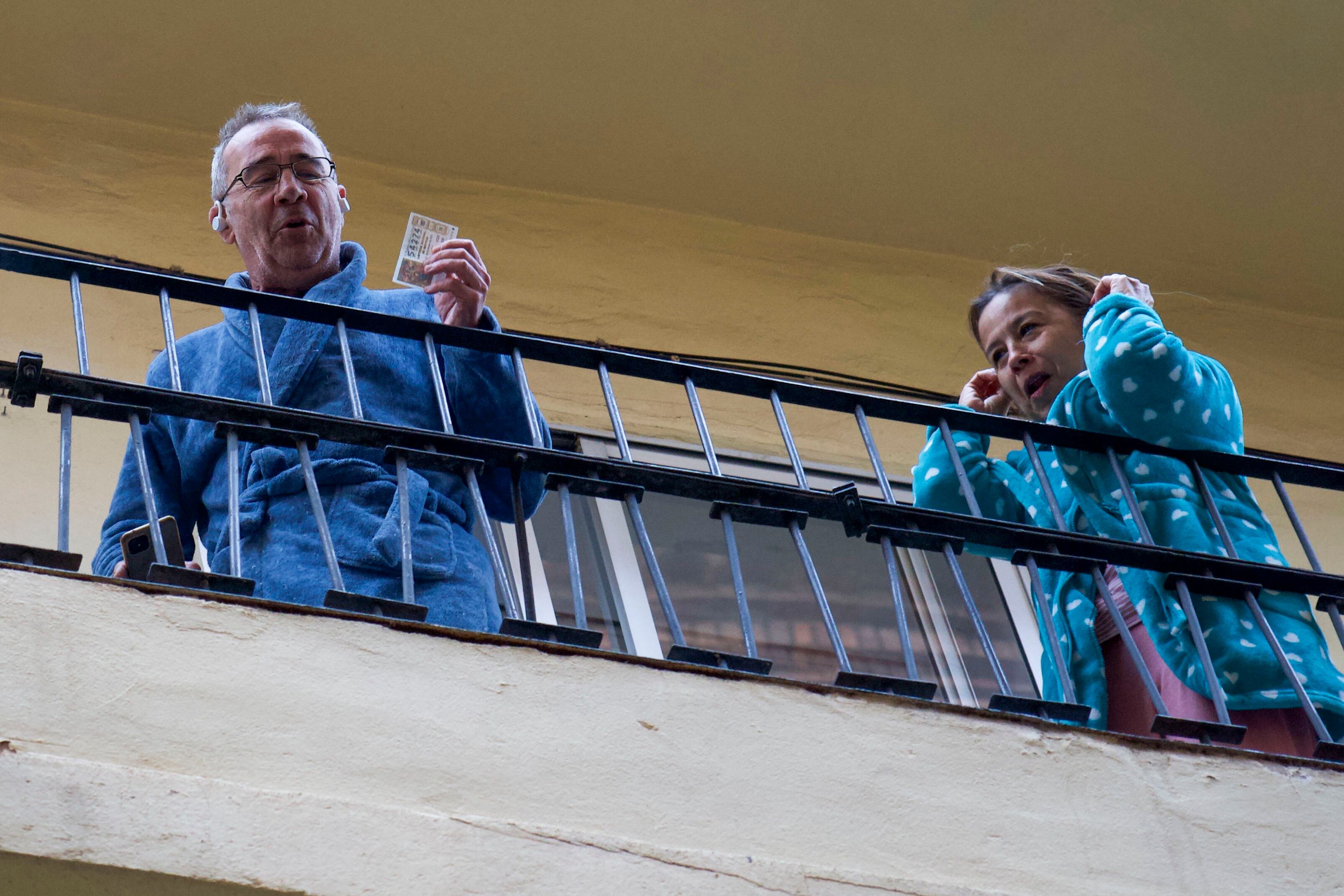 Dos de los premiados con el premio más madrugador de la mañana —el número 54274, el primer quinto premio repartido— han salido a la terraza de su vivienda a celebrar su suerte con albornoz y bata