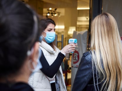 Una empleada de una tienda de moda en Pamplona toma la temperatura a una clienta a la entrada.