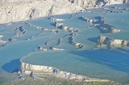 “Pamukkale” significa en turco “castillo de algodón” y da nombre a un blanco entramado de piscinas naturales de aguas termales, dispuestas en terrazas de piedra caliza y travertino que bajan, como cascadas petrificadas, por la ladera de una montaña. Esta famosa atracción se sitúa en la provincia de Denizli, en el suroeste de Turquía, y se salvó al ser declarada patrimonio mundial por la Unesco: había comenzado a ser invadida por hoteles que destruyeron parte de los restos de la antigua ciudad de Hierápolis, y estaba asolada por un turismo irresponsable. Los hoteles han sido demolidos, la rampa de asfalto construida a modo de acceso se ha cubierto de pozas artificiales donde darse un baño y está prohibido el uso de zapatos al pisar tanta blancura.