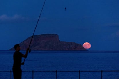 Un hombre pesca mientras aparece la superluna del Esturión este lunes en Islotes de las Cabras, Azores.  