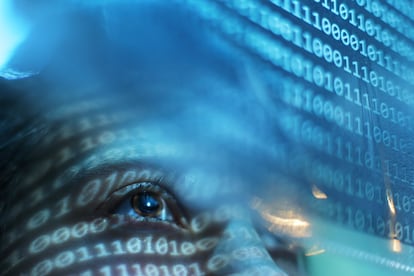 Una mujer mirando una pantalla azul iluminada con código binario.