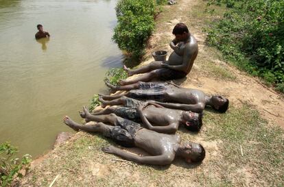 Un grupo de personas se relaja después de aplicarse una capa de barro sobre el cuerpo para refrescarse en un caluroso día de verano a orillas del lago Kanchon Mala en las afueras de Agartala, India.