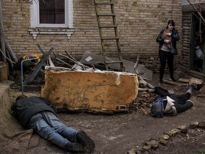 Una mujer pasa frente a varios cadáveres a las puerta de su casa en Bucha (Ucrania).