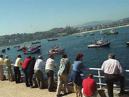 Un grupo de personas observa la concentración de barcos de la flota del Cantábrico en la bahía de La Concha, en San Sebastián.