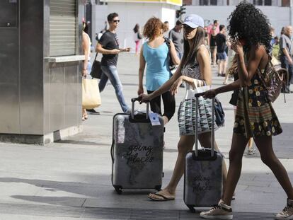 Dos jóvenes turistas camino de sus hospedajes en el centro de Madrid, con sus maletas caminando por la Puerta del Sol