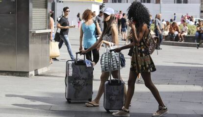 Dos jóvenes turistas camino de sus hospedajes en el centro de Madrid, con sus maletas caminando por la Puerta del Sol