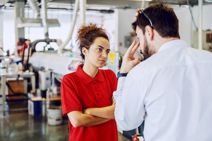 Serious cute caucasian female employee standing with arms crossed and listening angry director. Printing shop interior.