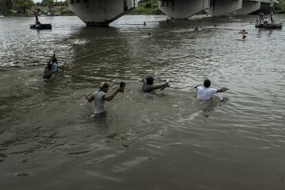 Um grupo de migrantes cruza o rio Suchiate e carrega seus sapatos nas mãos para que não se molhem.