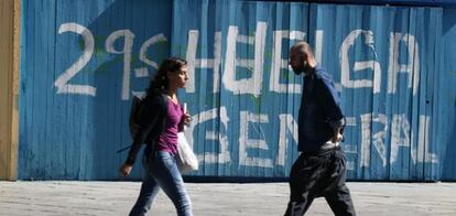 Dos viandantes delante de una pintada de la huelga general en la calle Fuencarral, del centro de Madrid.