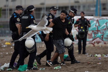 La policía portuaria acompañan a un joven que se niega a abandonar la playa de la Barceloneta. 
