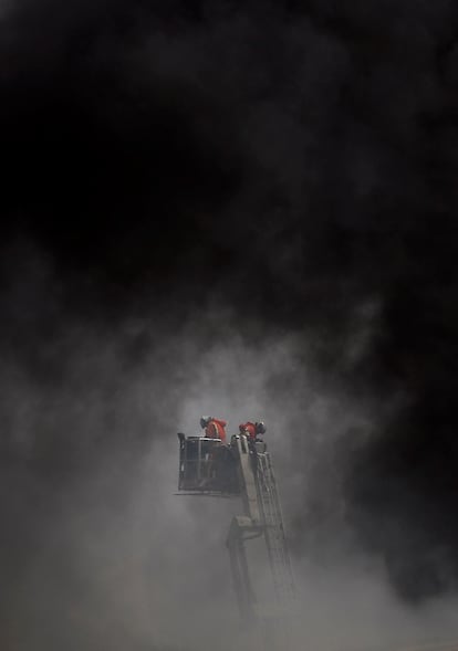 Dos bomberos trabajan este miércoles en el control y extinción del incendio declarado en una nave industrial de Aldaia (Valencia).