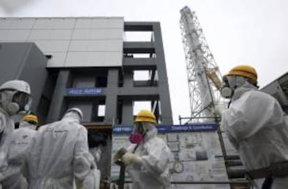 Empleados de Tokyo Electric Power (TEPCO) y periodistas se protegen con trajes y máscaras mientras pasan por delante del reactor 4 en la central nuclear de Fukushima, en Okuma (Japón) el pasado 7 de noviembre de 2013. EFE/Archivo