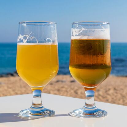Two beers of different tones in crystal glass on a sunny day in front of the beach